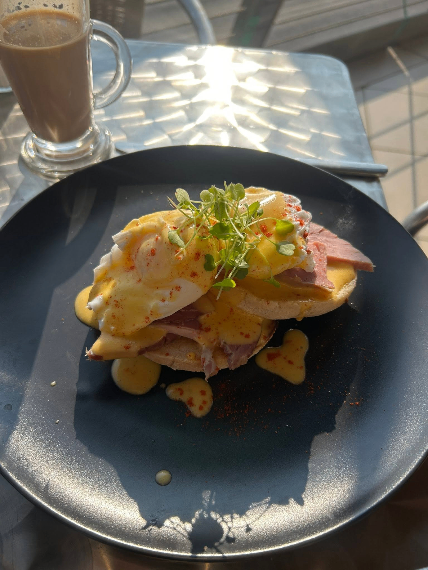 Eggs Benedict with ham, hollandaise and microgreens on a dark plate