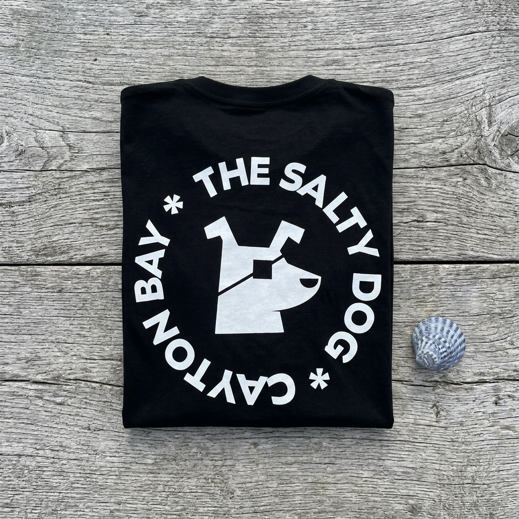 Black Salty Dog tee folded flat on driftwood with a seashell